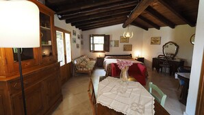 A cozy room with a wooden cabinet, a bed with floral bedding, a table with a lace tablecloth, and a hanging light fixture. - Glicine, romantic cottage with outdoor patio, on the hills of San Gimignano (San Gimignano)