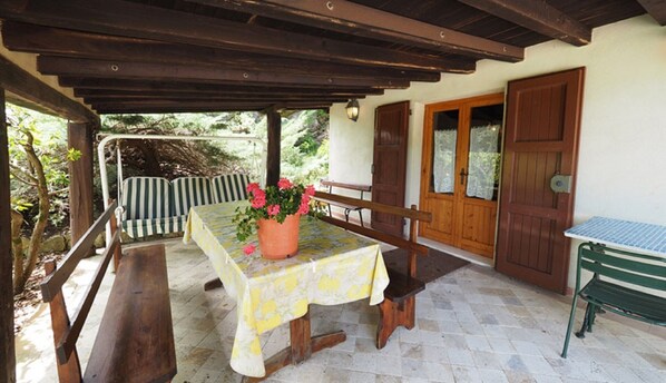 An outdoor patio with a table and benches, a potted plant, and a wooden door.
