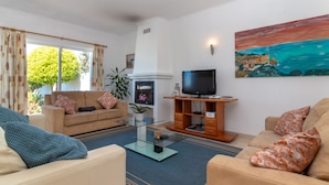 Uma sala de estar com um sofá, uma mesa de centro, uma TV sobre um suporte de madeira e um quadro na parede.