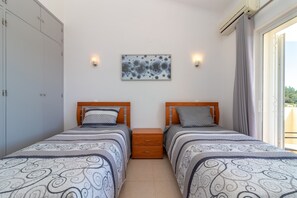 A bedroom with two beds, a nightstand, a wall-mounted artwork, and a window with curtains.
