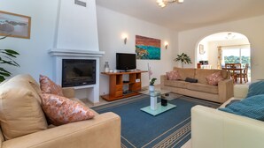 Sala de estar com lareira, sofá, televisão e área de jantar visível por um arco.