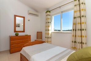 Ein Schlafzimmer mit einem Bett, einem Schminktisch, einem Spiegel und einem Fenster mit Vorhängen.