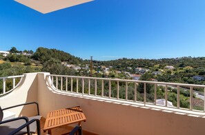 A balcony with a view of a residential area, a table, and chairs.