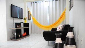Un salon comprenant un téléviseur, un canapé, un hamac et des vases décoratifs.