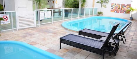 A swimming pool with lounge chairs, a covered area with a reception desk, and potted plants.