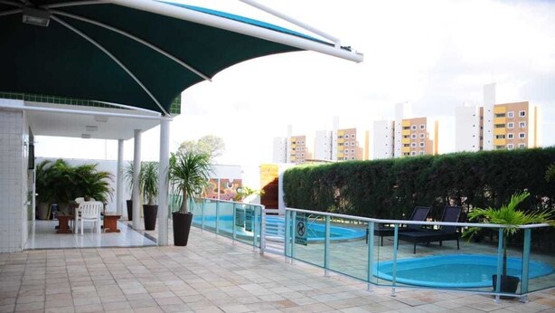Un espace piscine aménagé sur le toit, doté d’une rambarde en verre, de chaises longues et de plantes en pot.