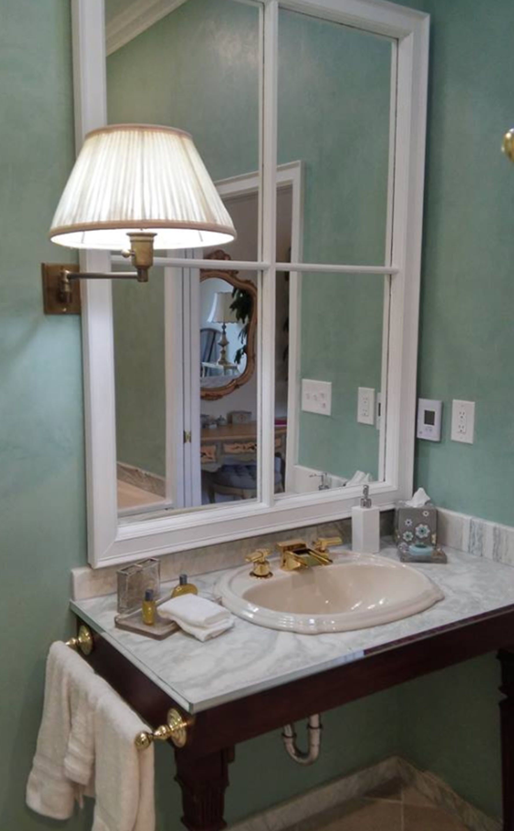 A bathroom with a vanity, sink, mirror, and a wall-mounted lamp.