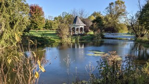 A tranquil pond with a gazebo, surrounded by lush greenery and trees. - Inntiquity A Country Inn (Logansport)