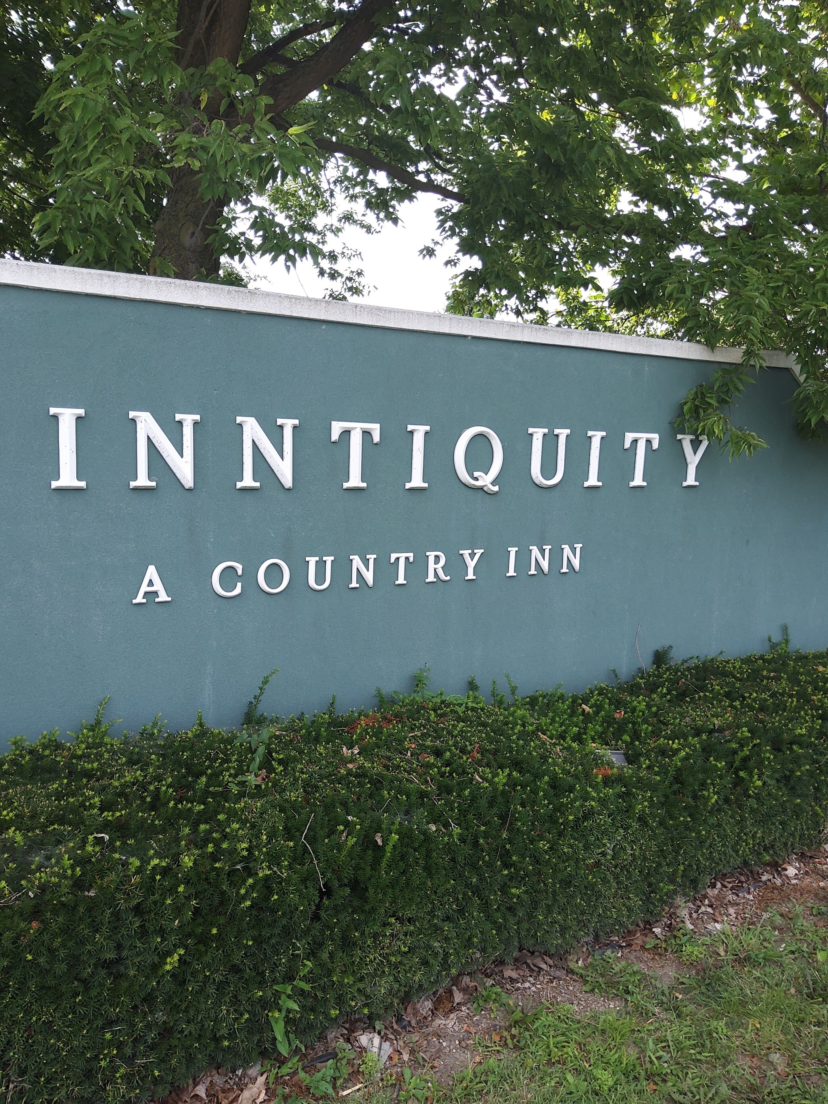 A sign for InnTiquity, a country inn, with a green wall and white lettering.