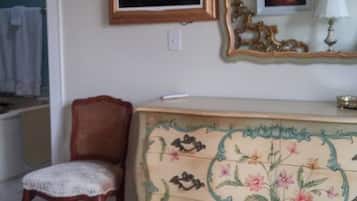 Un dormitorio con una silla de madera, un aparador con motivos florales, un espejo de marco ornamentado y una lámpara de araña.