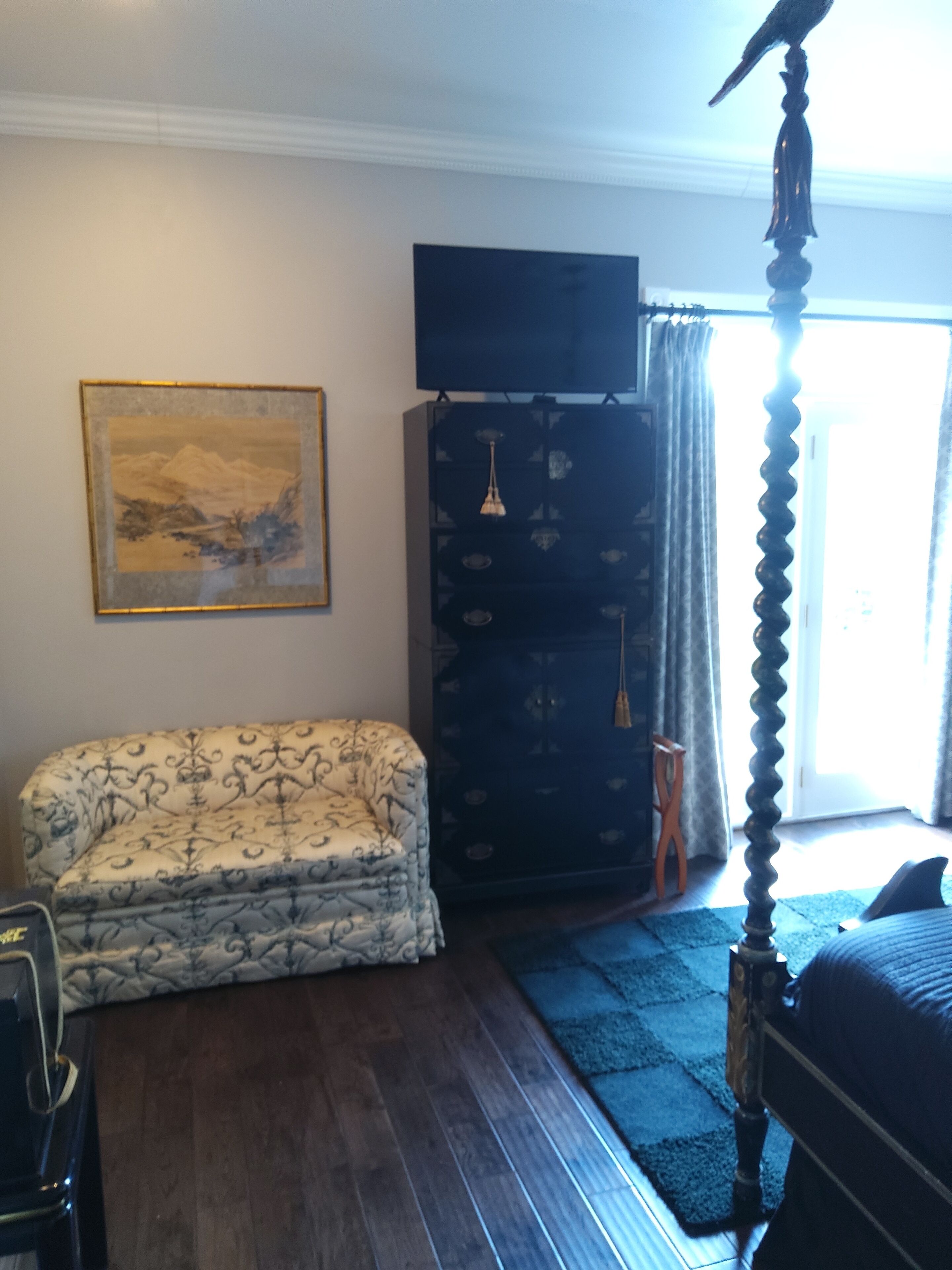 A room with a bed, a chair, a TV, a painting, and a wardrobe.