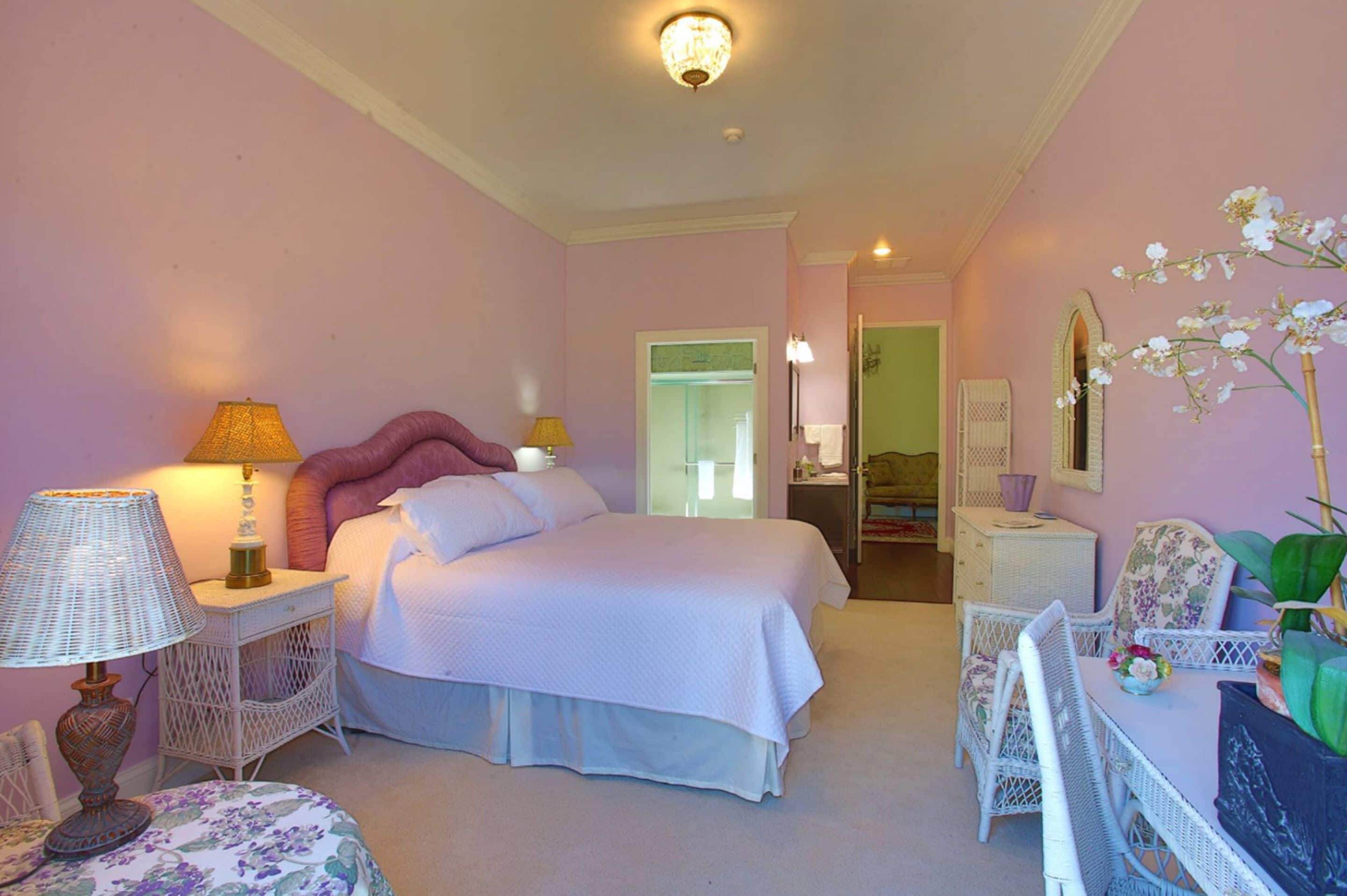 A bedroom with a bed, bedside tables, a chair, a table, and a mirror.