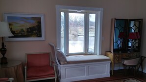 A room with a window seat, a chair, a table, a lamp, a dresser, and a painting. - Inntiquity A Country Inn (Logansport)