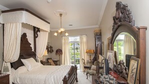 A bedroom with a four-poster bed, a wooden dresser, a mirror, and a view of the garden through a window. - Inntiquity A Country Inn (Logansport)