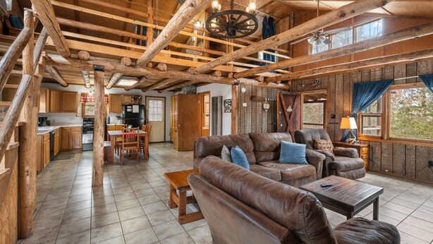A spacious living area with a large leather sofa, wooden beams, and a view of the kitchen and dining area. - Rustic, close to buffalo river, secluded getaway, king bed, hiking ,WIFI (Jasper)