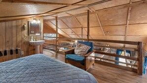 A wooden interior with a bed, a chair with a cushion, a sink, and a window overlooking a balcony. - Rustic, close to buffalo river, secluded getaway, king bed, hiking ,WIFI (Jasper)