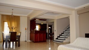 Amplia sala de estar con mesa de comedor, sillas, sofá, zona de cocina y una escalera.