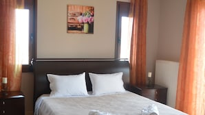 Una cama bien tendida con sábanas blancas y dos toallas enrolladas, una mesita de noche con lámpara, y un cuadro en la pared.