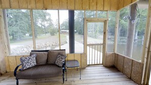 A wooden porch with a cushioned bench and a small table, large windows offering a view of a natural landscape. - Waterfront Retreat in Toledo Bend (Many)