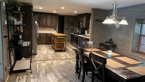 A modern kitchen with wooden cabinets, a central island, and a dining area with a table and chairs. - Waterfront Retreat in Toledo Bend (Many)
