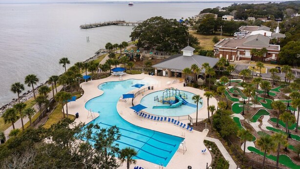 A large outdoor swimming pool with a water slide, surrounded by palm trees and a view of the ocean. - St. Simons Island secret! (St Simons Island)