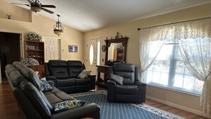 A living room with a sofa, two recliners, a coffee table, a patterned rug, and a large window with curtains. - Custom home great local, boat parking,  near dock, food, scalloping,  Manatee. (Homosassa)