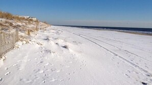 Una spiaggia innevata con impronte e una recinzione di legno.