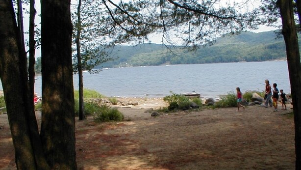 A natural setting with a lake and trees, a sandy area, and people in the background. - Private Dock in Protected Cove (Edinburg)