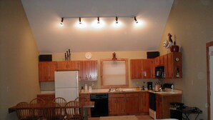 A compact kitchen with wooden cabinets, a white refrigerator, and a dining area with a white sofa and wooden chairs. - Private Dock in Protected Cove (Edinburg)