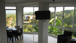 A spacious room with a large balcony, a bed, a TV, and a dining area with chairs and a table. - Casa Papillon: Waterfall pool, Jungle Views, Terrace, Sleeps 12 (Manuel Antonio)