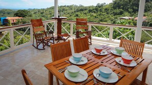 A wooden table set with bowls and plates, surrounded by chairs, on a balcony with a view of a lush green landscape. - Casa Papillon: Waterfall pool, Jungle Views, Terrace, Sleeps 12 (Manuel Antonio)