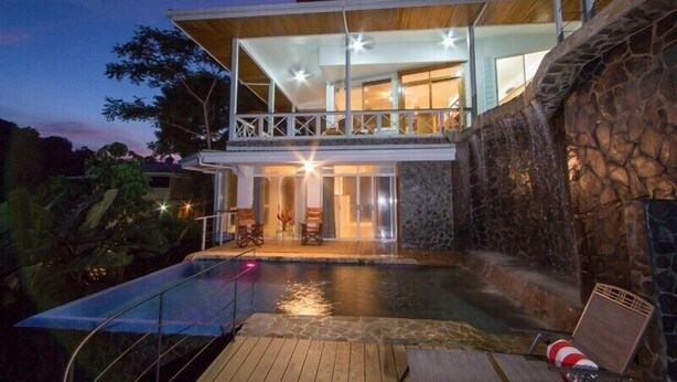 A modern house with a swimming pool, stone walls, and a balcony overlooking the pool. - Casa Papillon: Waterfall pool, Jungle Views, Terrace, Sleeps 12 (Manuel Antonio)