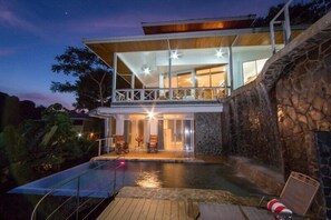 A modern house with a swimming pool, stone walls, and a balcony overlooking the pool. - Casa Papillon: Waterfall pool, Jungle Views, Terrace, Sleeps 12 (Manuel Antonio)