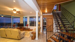 A spacious living room with a sofa, a TV, and a staircase leading to an upper level. - Casa Papillon: Waterfall pool, Jungle Views, Terrace, Sleeps 12 (Manuel Antonio)