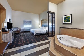 A hotel room with a bed, a desk with a computer, a large bathtub, and a television. - Holiday Inn Amarillo East by IHG (Amarillo)