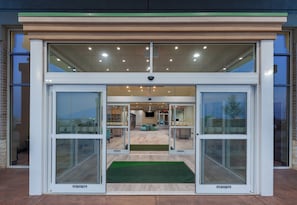 A modern building entrance with automatic sliding doors, a green mat at the entrance, and a view into the interior which includes seating areas and a reception desk. - Holiday Inn Amarillo East by IHG (Amarillo)