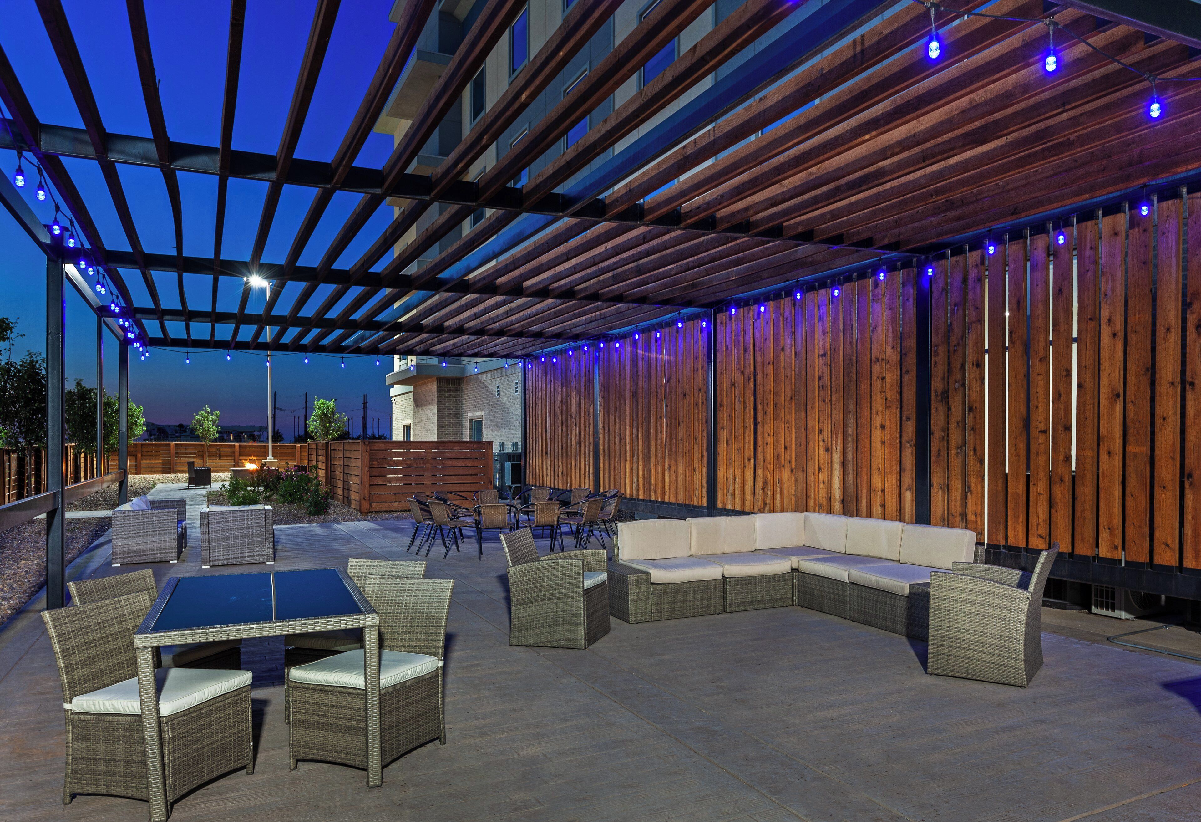 Een terras met een houten pergola, rieten meubels en een zithoek.