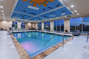 An indoor swimming pool with clear water, surrounded by lounge chairs and a ceiling with a sun and cloud design. - Holiday Inn Amarillo East by IHG (Amarillo)
