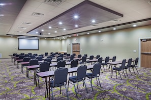 A conference room with rows of tables and chairs, a projector screen, and a door. - Holiday Inn Amarillo East by IHG (Amarillo)