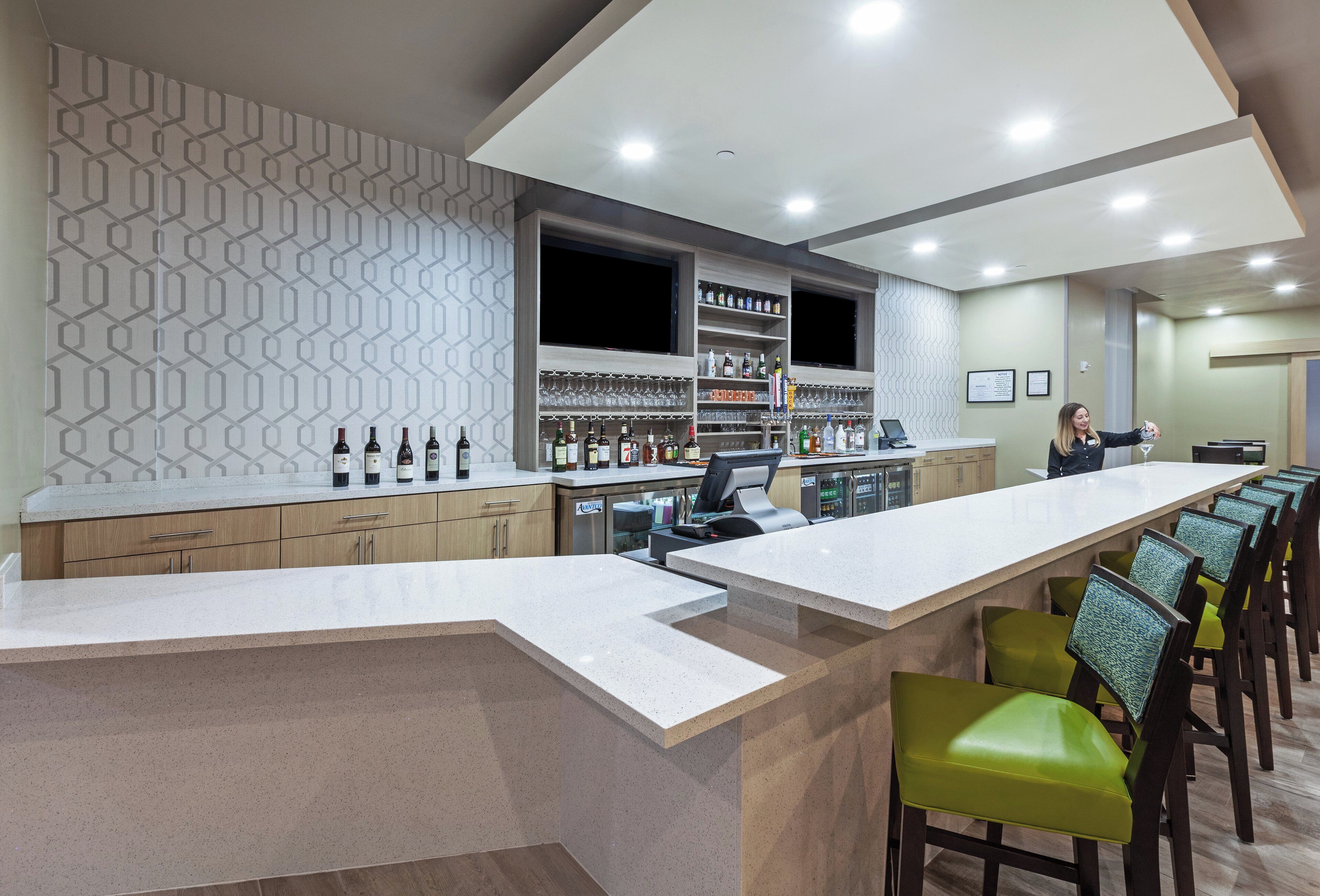 A bar area with a long counter, shelves with bottles, and a seating area with chairs.