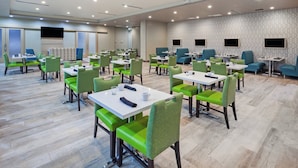 A hotel dining area with multiple tables and chairs, a flat-screen TV mounted on the wall, and a patterned wall design. - Holiday Inn Amarillo East by IHG (Amarillo)