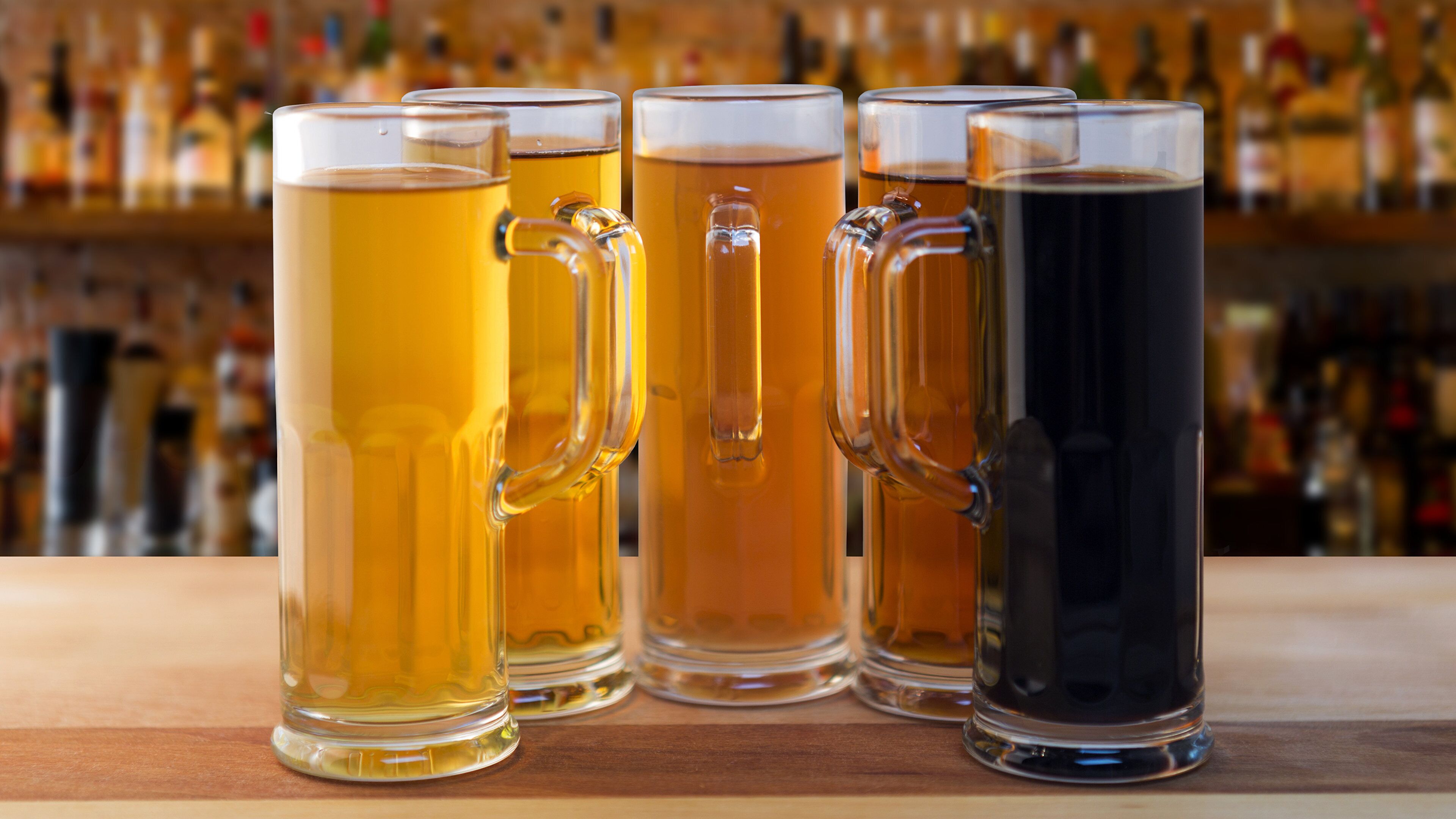 A row of beer mugs on a bar counter with a blurred background of bottles.