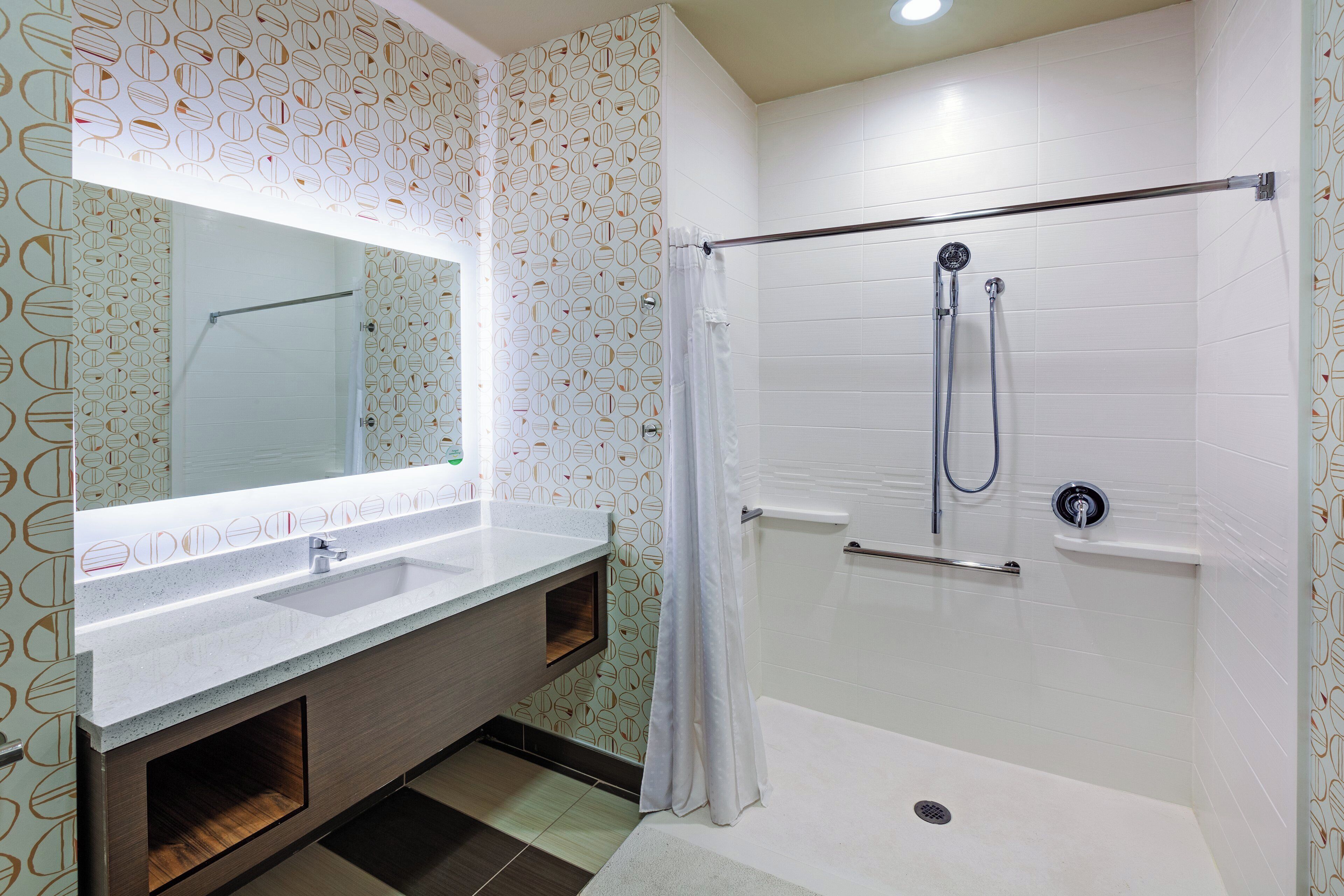 Un baño moderno con ducha, tocador con espejo y pared con estampado.