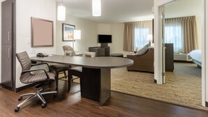 A hotel room with a large desk, office chairs, a flat-screen TV, a sofa, and a bed.
