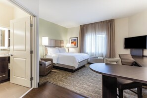 Habitación de hotel con cama, mesita de noche, lámpara, televisión y escritorio con silla.