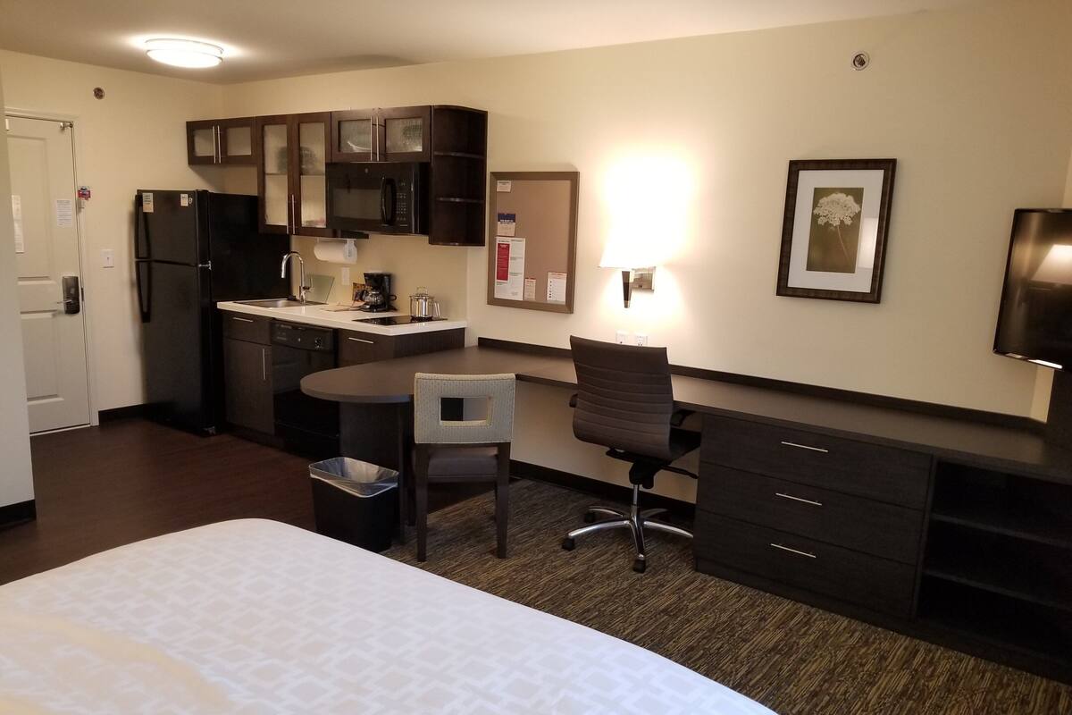 Une chambre d’hôtel équipée d’un lit, d’un bureau, d’une chaise, d’un four à micro-ondes, d’un réfrigérateur, d’un lavabo et d’une poubelle.