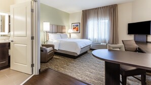 A hotel room with a bed, bedside table, lamp, TV, and a desk with chairs.