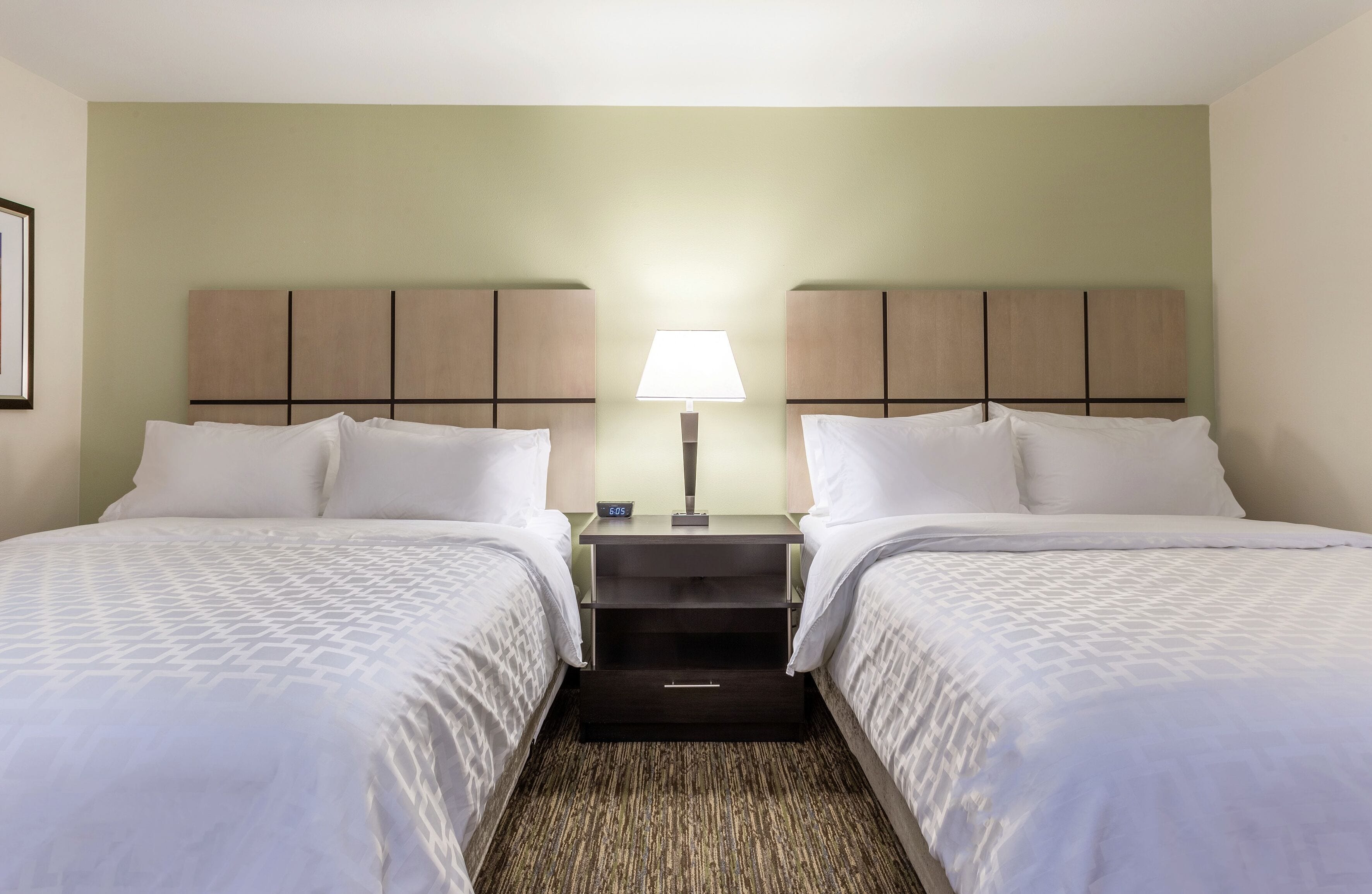 A hotel room with two beds, a nightstand with a lamp, and a small drawer.