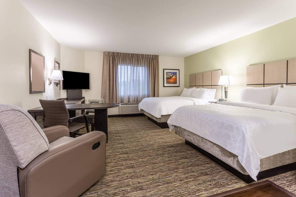 Une chambre d’hôtel avec deux lits, un bureau, une chaise, une télévision et une fenêtre avec des rideaux.
