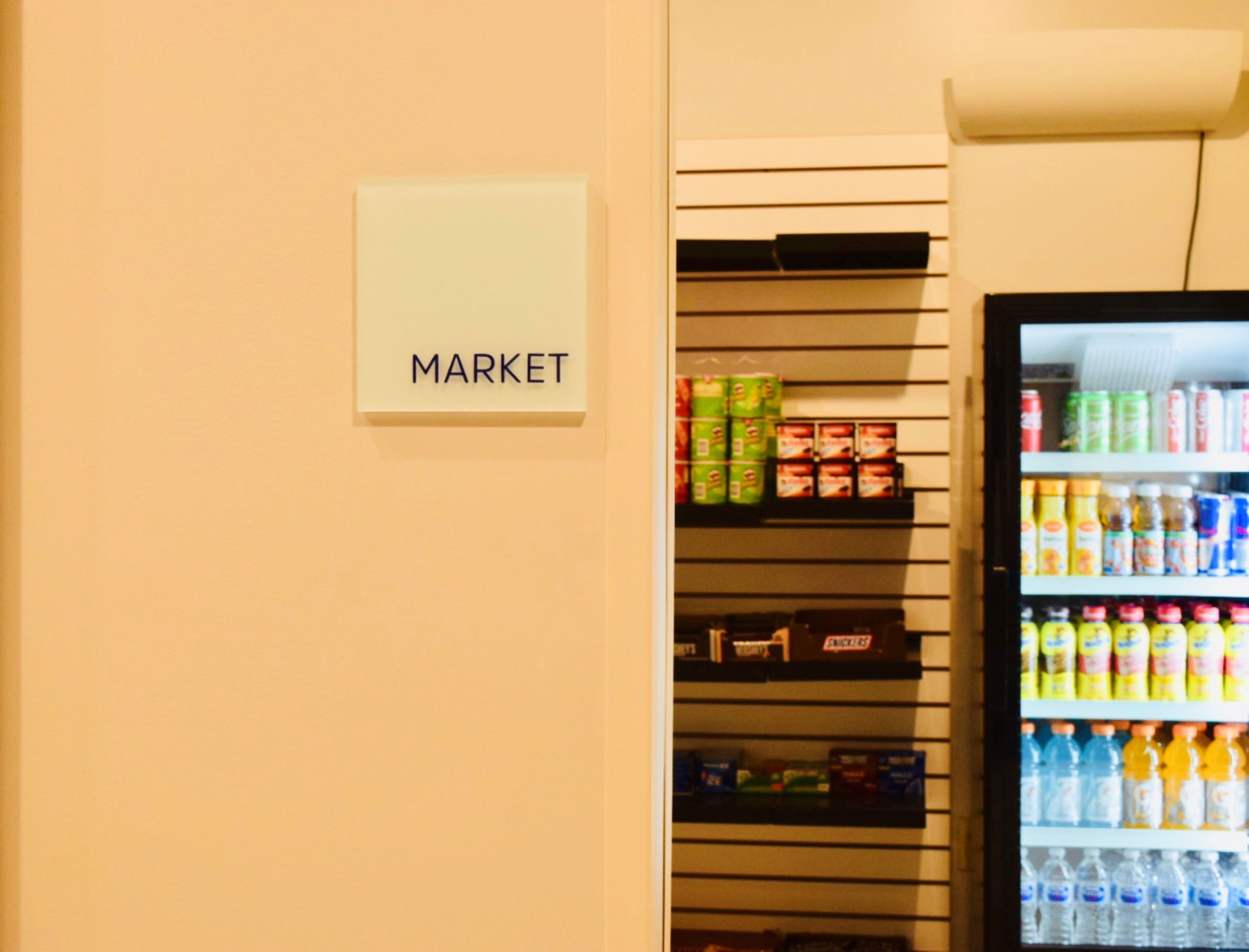 Ein Verkaufsautomat mit verschiedenen Getränken und Snacks, ein Regal mit verpackten Waren und ein Schild mit der Aufschrift 'MARKET'.